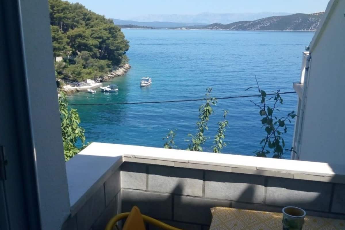 A balcony with a table and a chair, overlooking a body of water with boats and a coastline.