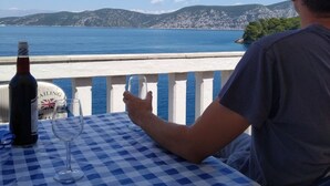 A person seated at a table with a checkered tablecloth, holding a wine glass, with a bottle of wine and a sign reading "Richmonds Sailing Club" in the background. - Apartments Ivo (Korčula)