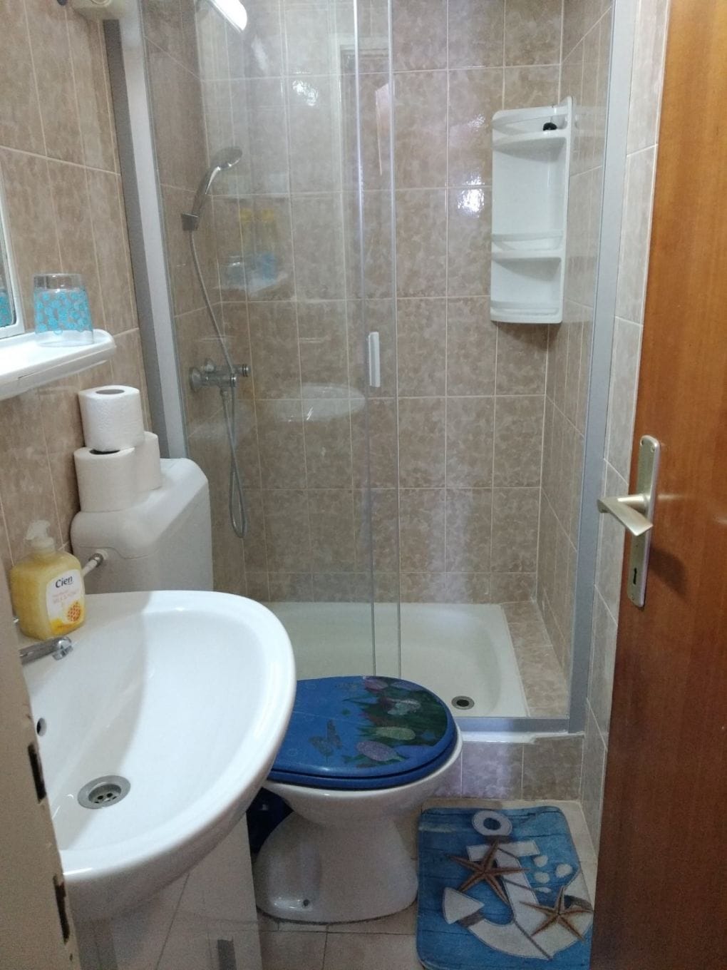 A bathroom with a shower, toilet, sink, and a small shelf with toiletries.