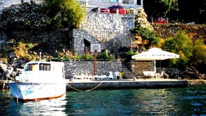 A coastal building with a stone facade, a balcony, and a small pool area with chairs and an umbrella. - Apartments Ivo (Korčula)
