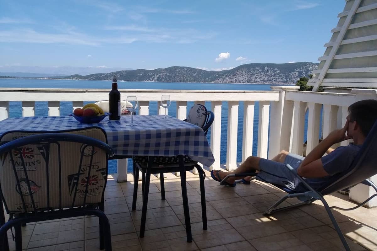 A balcony with a table set for two, a bottle of wine, and a bowl of fruit.