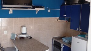 A compact kitchen with blue cabinets, a built-in microwave, a coffee maker, and a small refrigerator. - Apartments Ivo (Korčula)