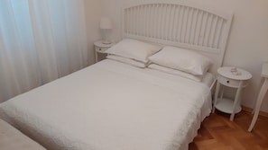 A white bed with a headboard, two bedside tables, and a small shelf. - Apartment Kline (Makarska)