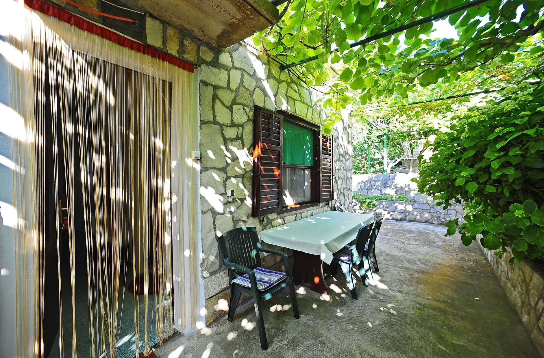 A stone building with a table and chairs outside, surrounded by greenery.
