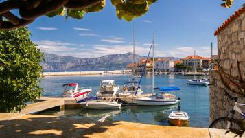 Un puerto deportivo con barcos amarrados, un muro de piedra y vistas a montañas al fondo.