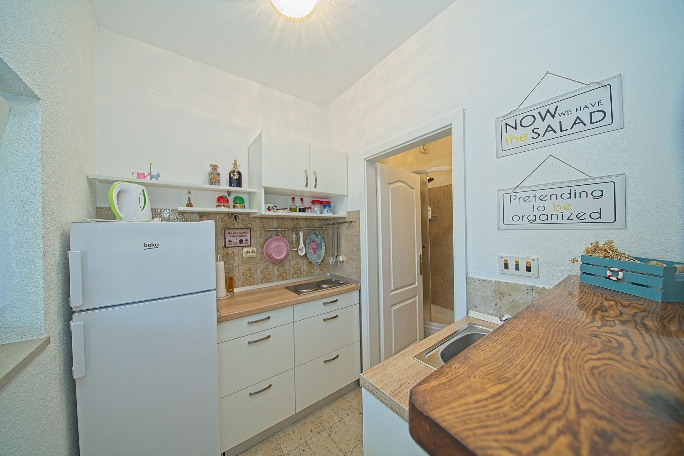 A compact kitchen with a refrigerator, cabinets, and a countertop. There are signs on the wall and a small sink.