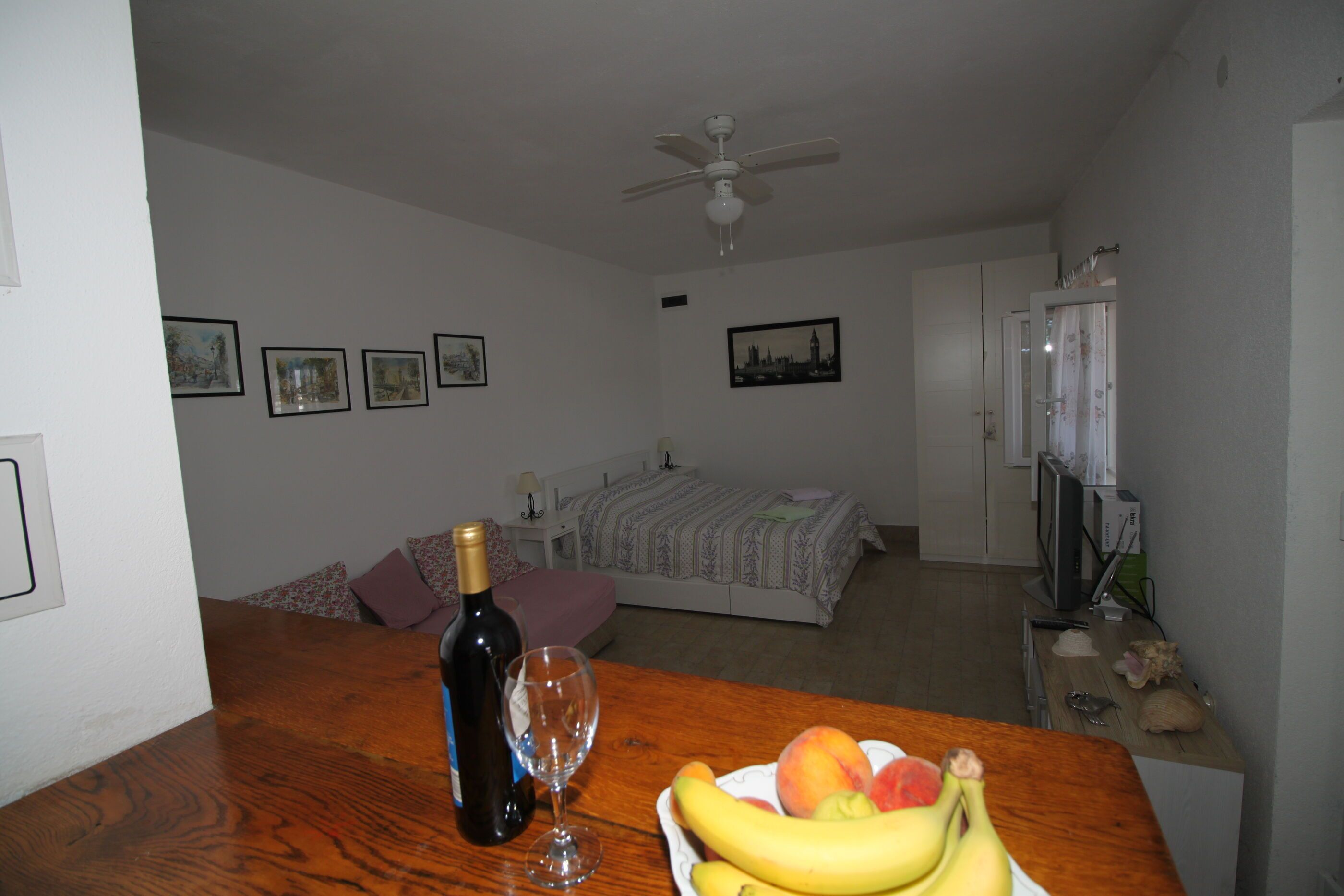 Ein Zimmer mit einem Bett, einem Fernseher, einer Weinflasche und einer Obstplatte auf einem Tisch.