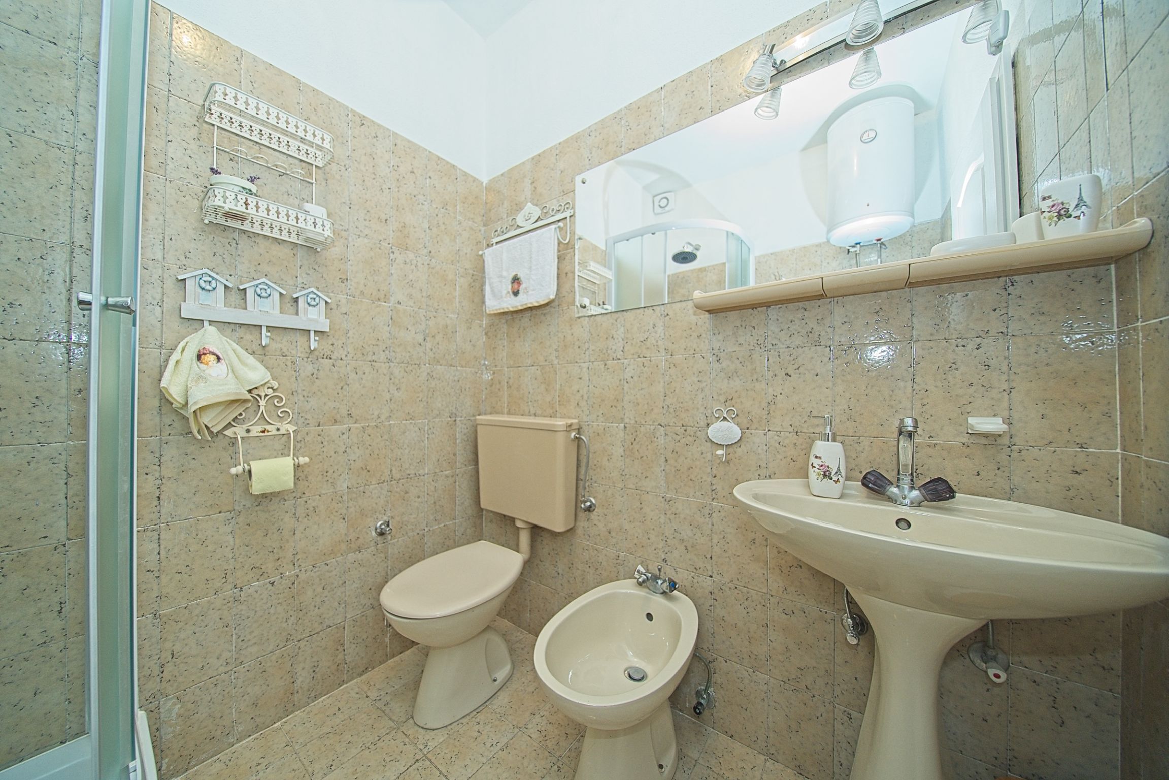 A bathroom with a toilet, bidet, and sink, tiled walls, and a mirror.