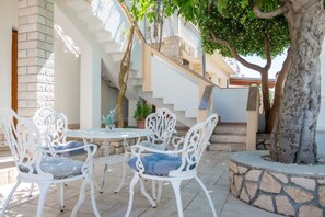 An outdoor patio with white metal chairs and a round table, surrounded by stone walls and a staircase. - Apartment Luca (Povljana)