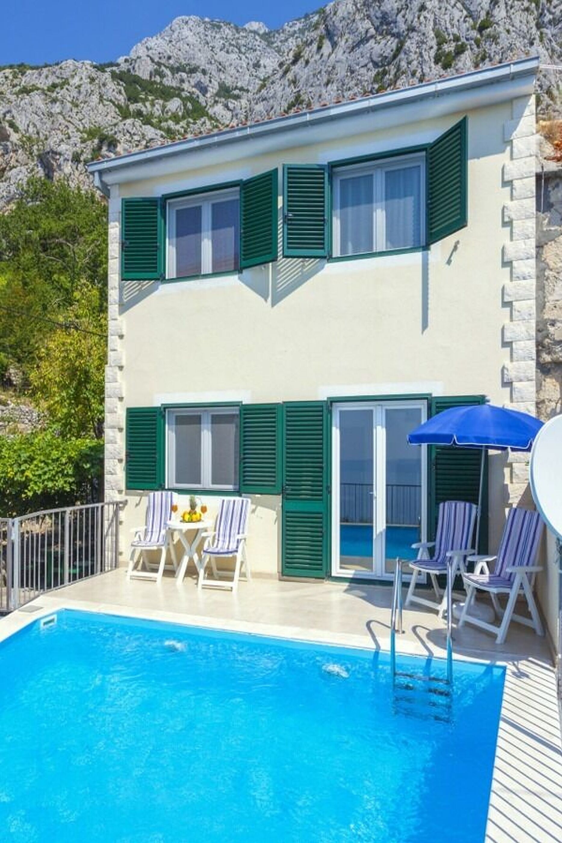 A two-story building with a swimming pool, outdoor seating, and a mountain backdrop.