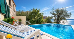 A swimming pool with lounge chairs, a potted plant, and a view of the sea. - House Ned (Tucepi)