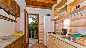 A kitchen with wooden cabinets, a white refrigerator, a stove, and a sink. There is a balcony with a railing and a view of trees. - Apartment Kati (Hvar)