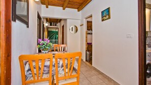 A hallway with a wooden ceiling, a dining table with chairs, a potted plant, and a door with a number sign. - Apartment Kati (Hvar)