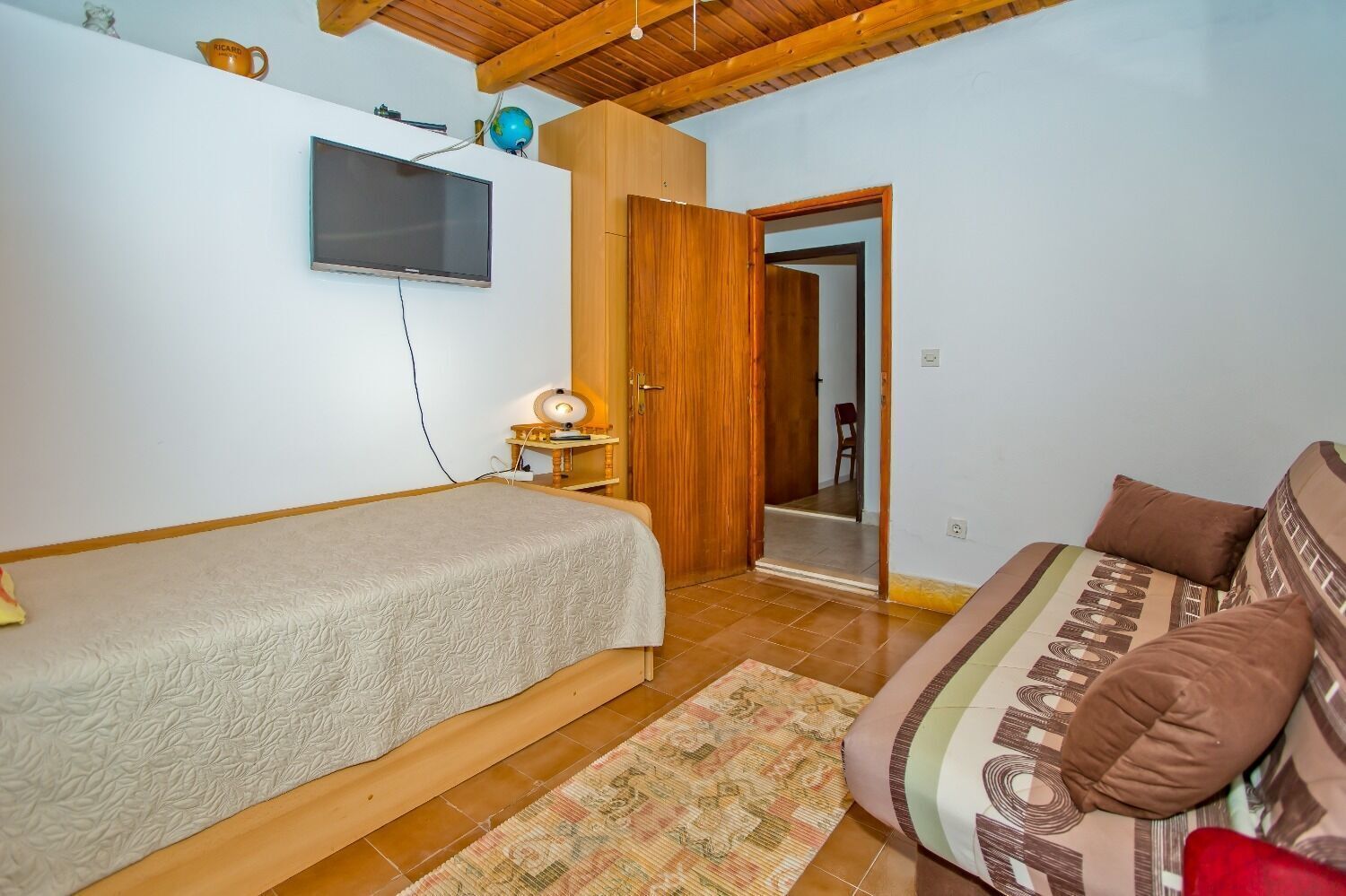 Quarto com cama, sofá, televisão e armário de madeira.