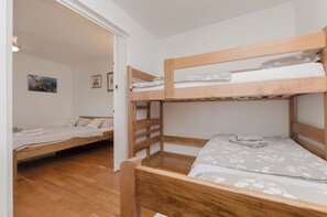 A bunk bed room with a wooden floor, a door leading to another room, and a wall with framed pictures. - Apartments Ema (Murter-Kornati)