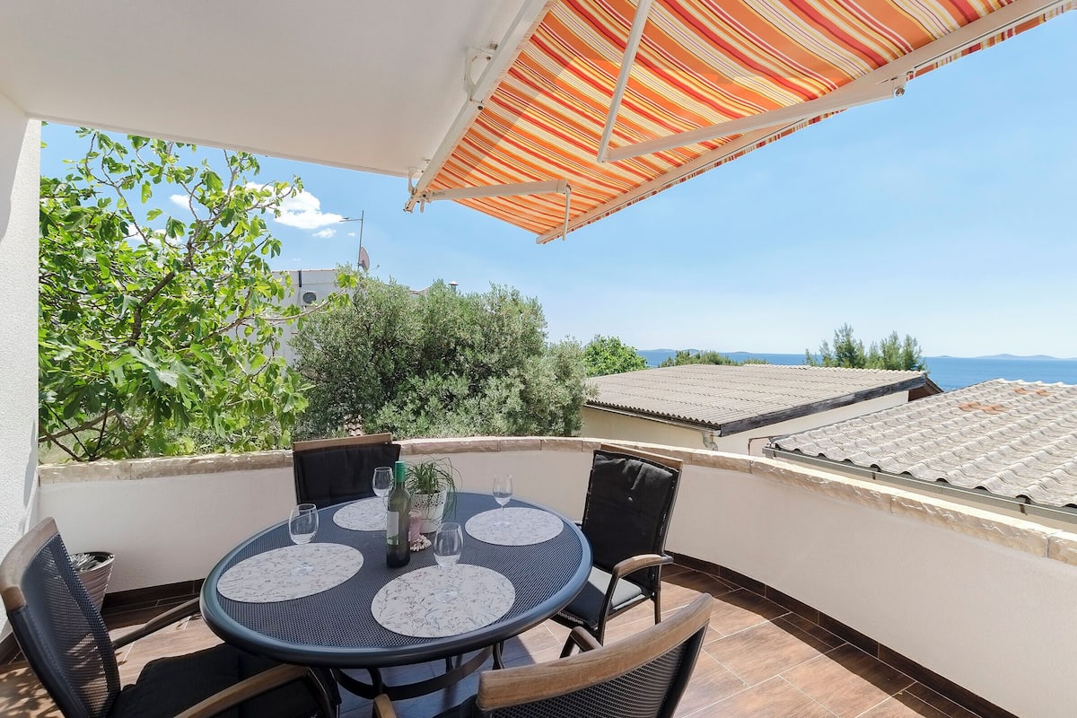 A balcony with a round table, chairs, and a striped awning.