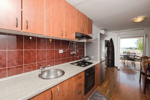 Une cuisine avec des meubles en bois, une cuisinière à gaz, un évier et une vue sur l’extérieur.