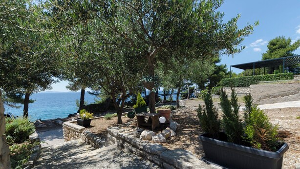 Ein gepflasterter Weg führt zu einer Sitzgruppe mit Blumentöpfen und Blick auf das Meer.