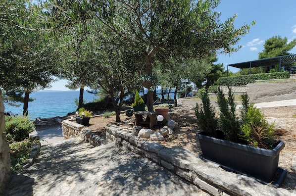 A stone pathway leading to a seating area with potted plants and a view of the sea. - Apartments Ema (Murter-Kornati)
