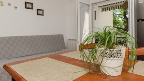 Ein Zimmer mit einem Holztisch, einem grauen Sofa mit Muster, einer weißen Wand mit gerahmten Bildern und einer Topfpflanze.