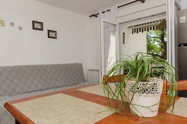 A room with a wooden table, a potted plant, a grey patterned sofa, and a white wall with framed pictures. - Apartments Ema (Murter-Kornati)
