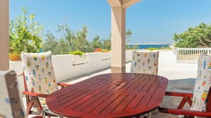 Un espace extérieur abrité, avec une table et des chaises rouges, offrant une vue panoramique sur la mer.