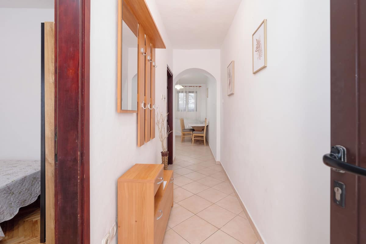 Un pasillo con un armario de madera, un espejo y una puerta que da a una habitación con cama y mesa.