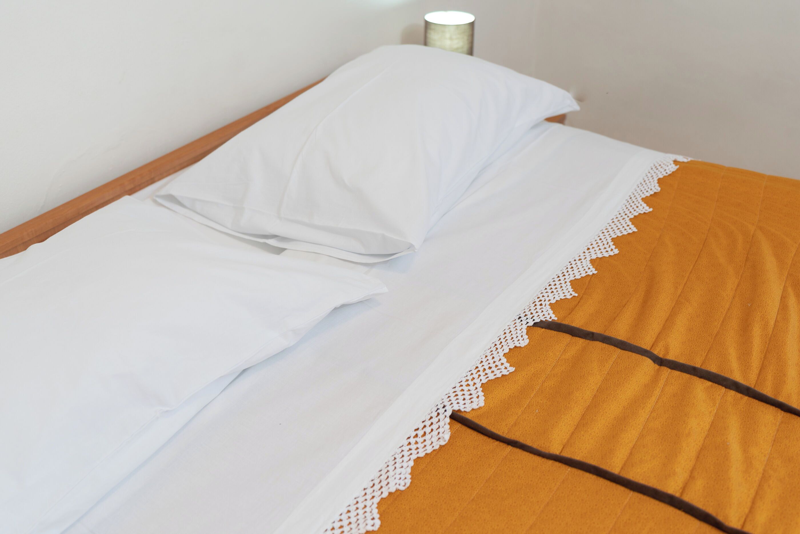 Een bed met witte lakens en een bruine deken met kant.