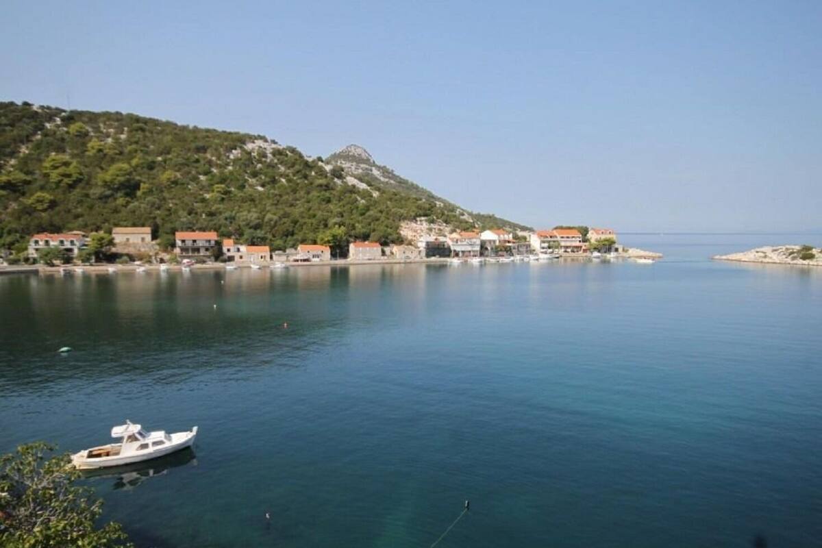 A coastal town with buildings along the water, a boat docked near the shore, and a hill in the background.