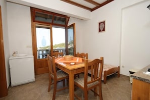 A compact dining area with a wooden table and chairs, a small refrigerator, and a sliding glass door leading to a balcony. - Apartment Milan (Lastovo)