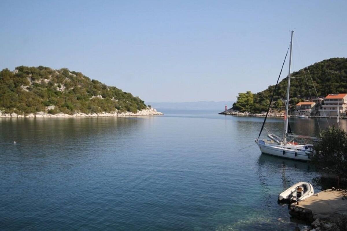 A calm bay with a sailboat docked near the shore, surrounded by hills and a clear sky.
