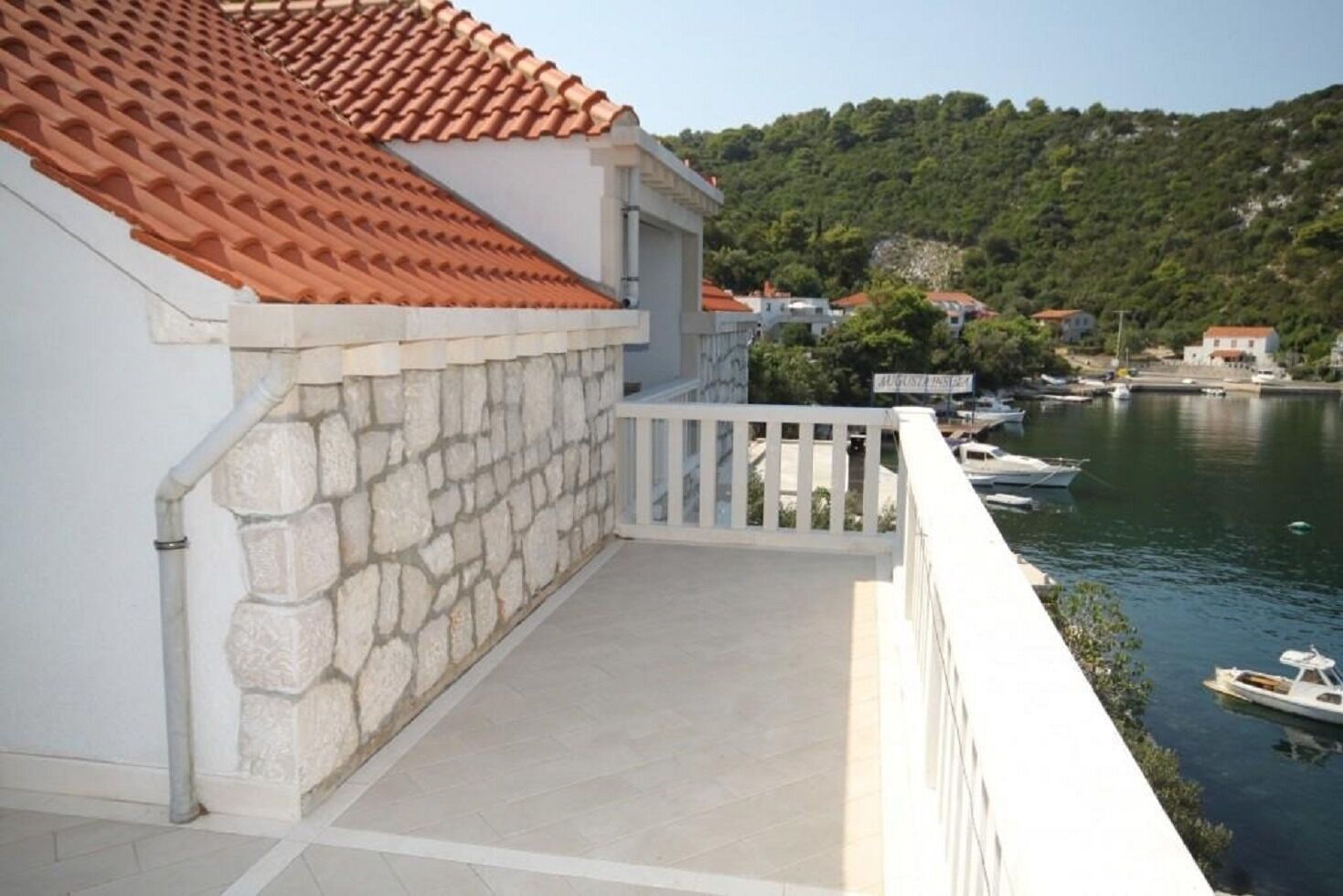 A balcony with a stone wall and a red-tiled roof overlooking a body of water with boats.