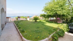A garden with a pathway leading to a building, surrounded by greenery and a clear view of the sea. - Apartment Orange (Postira)