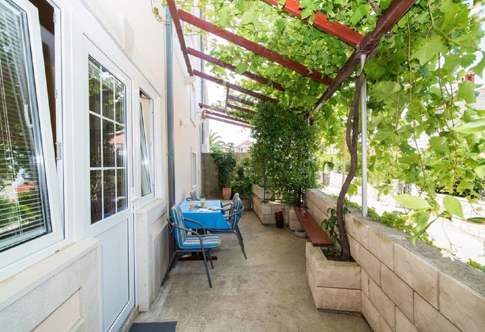 A covered patio with a table and chairs, potted plants, and a pergola with vines.