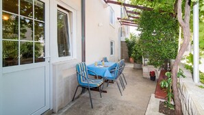 A covered patio with a table and chairs, a pergola with vines, and a small tree. - Apartment Orange (Postira)
