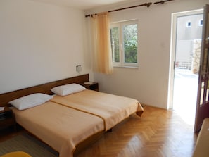 Quarto com cama de madeira, mesa de cabeceira, abajur e janela com cortinas.