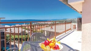 Un balcone con tavolo e sedie, una ciotola di frutta e vista sul mare e sulla città.
