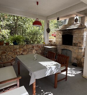 Eine Terrasse im Freien mit einer Steinmauer, einem Tisch mit Stühlen und einem Holzofen.