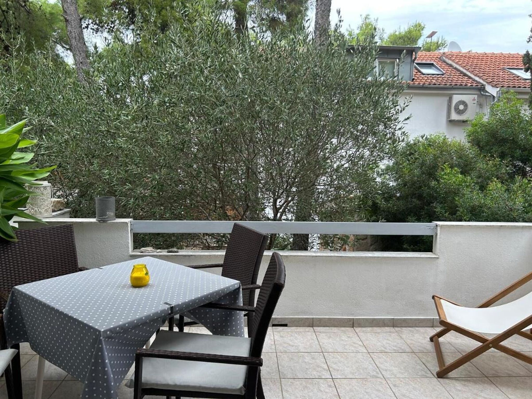 An outdoor patio with a table and chairs, surrounded by greenery and a building in the background.