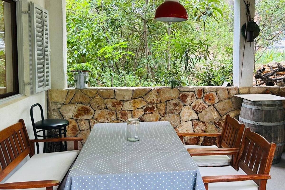 A covered patio with a stone wall, a table with a polka dot tablecloth, wooden chairs, and a red pendant light.