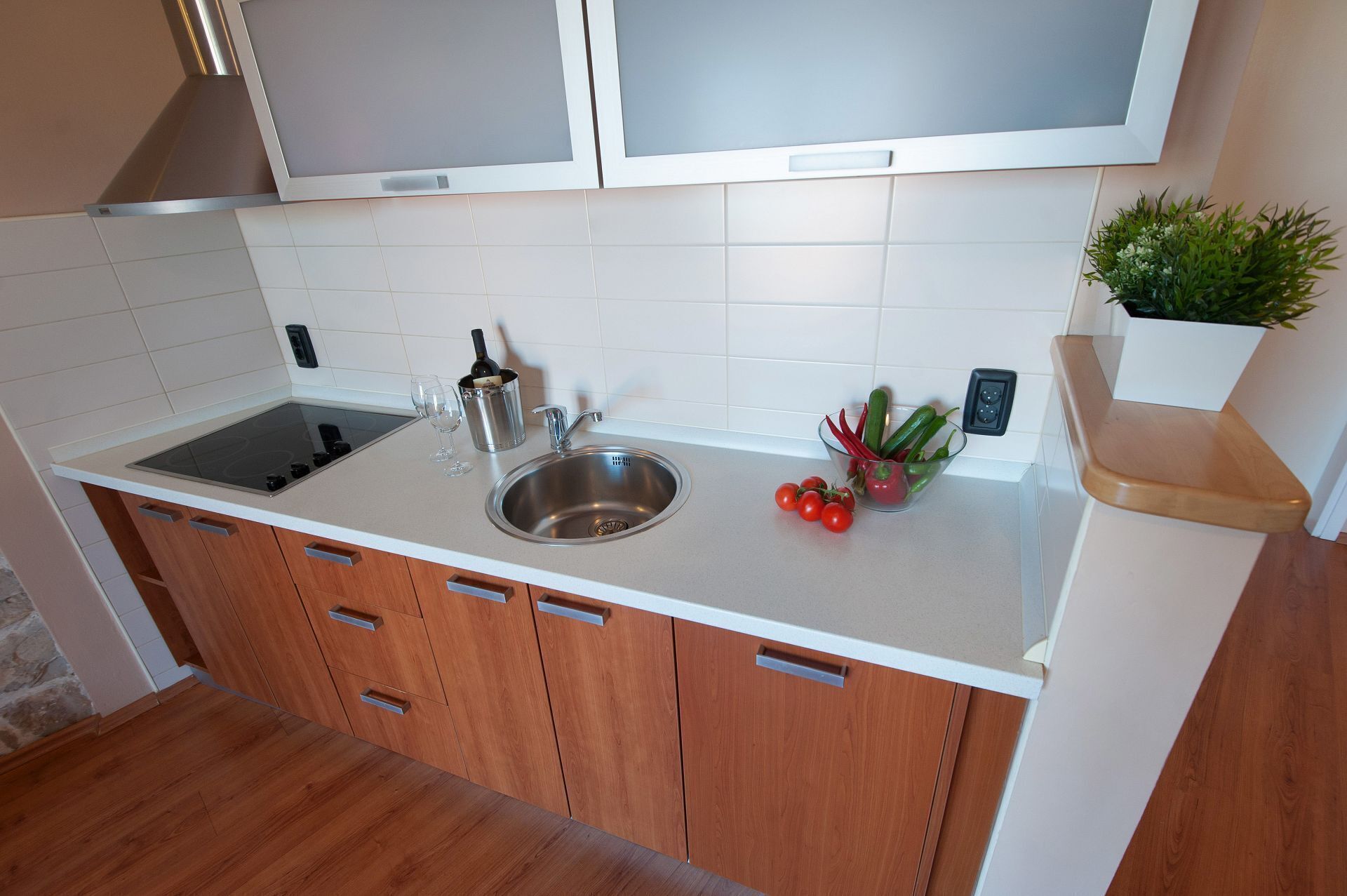 A modern kitchen with a stainless steel sink, a built-in stove, wooden cabinets, and a small potted plant on the countertop.