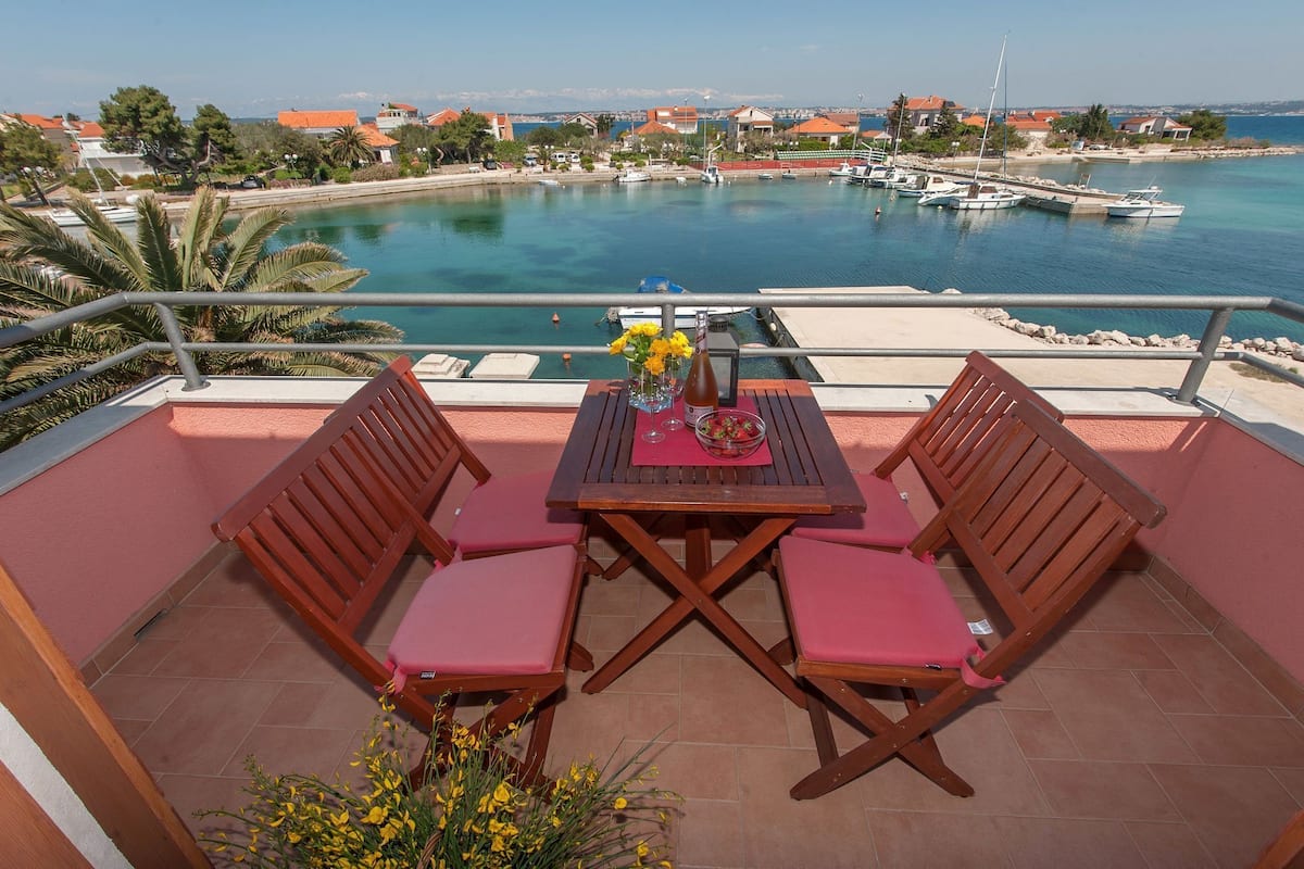 A terrace with a table, two chairs, a bottle, and a bowl of strawberries.