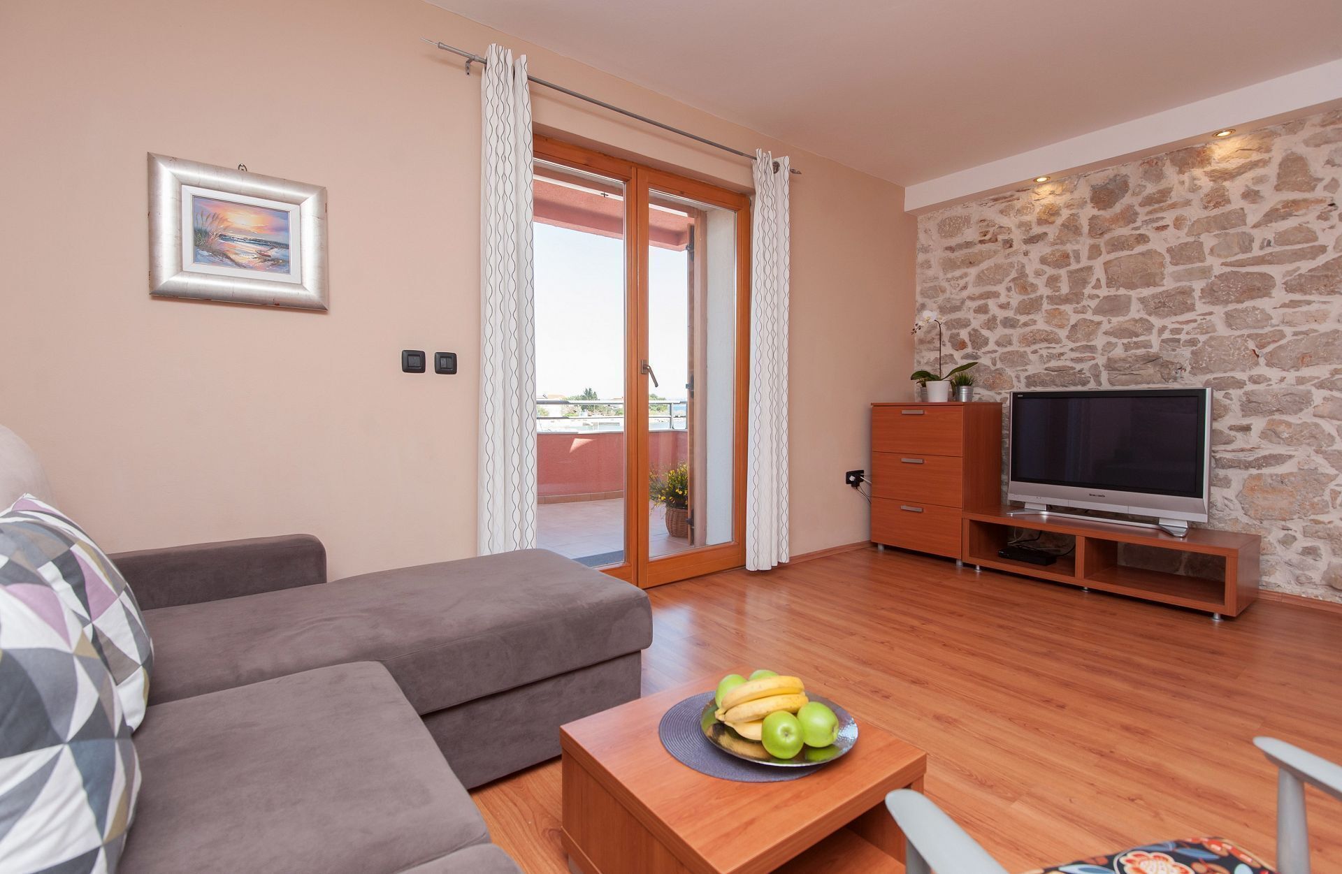 A living room with a sofa, a TV, a fruit bowl, and a stone wall.