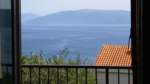 A view from a balcony with a tiled roof and a railing, overlooking a body of water and distant mountains. - Apartment Griv (Cres)