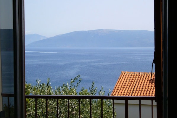 A view from a balcony with a tiled roof and a railing, overlooking a body of water and distant mountains. - Apartment Griv (Cres)