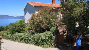 A coastal house with a red-tiled roof, a visible chimney, and a garden with flowering bushes. - Apartment Griv (Cres)