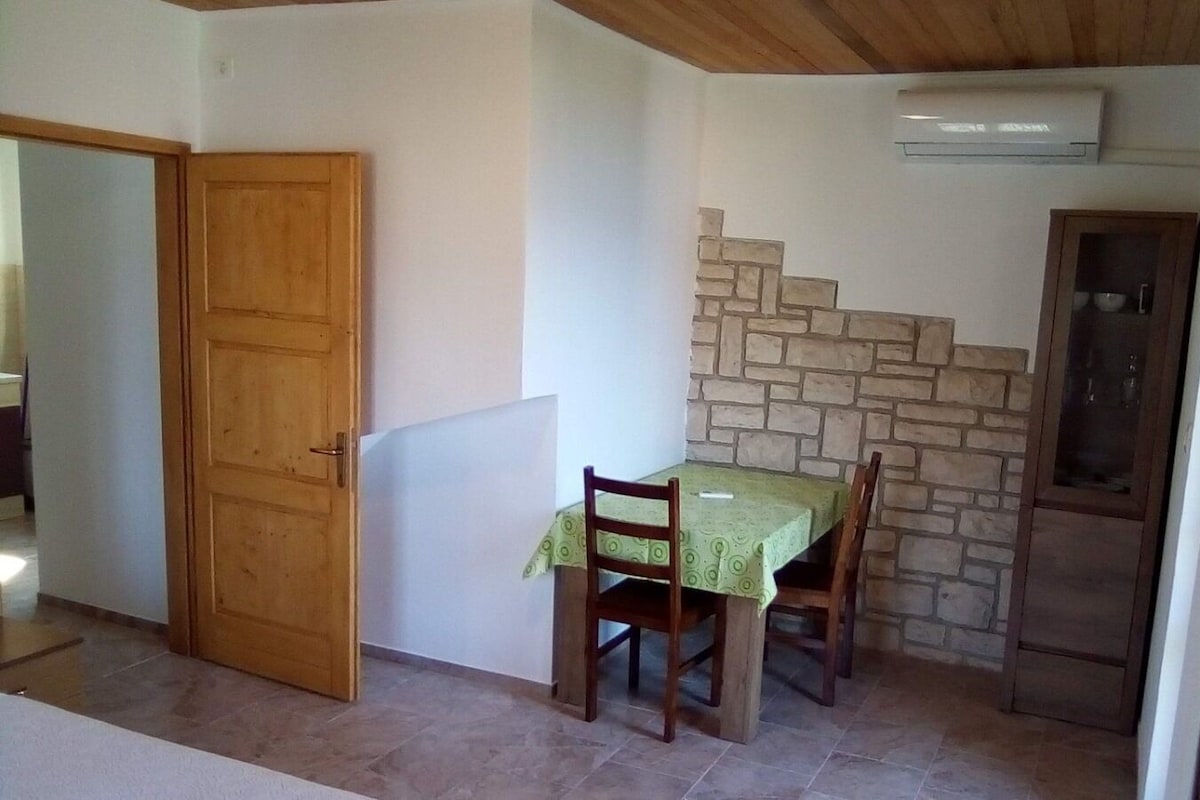 Un coin repas avec une table et des chaises, une porte en bois, un mur en pierre et un réfrigérateur.