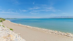 Une plage à l’eau d’un bleu limpide, un mur de pierres et des montagnes à l’horizon.