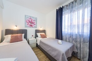 A hotel room with two beds, a nightstand, a painting of a flower, and a window with sheer curtains. - Apartments Dreamy (Nin)