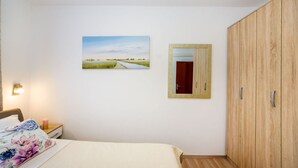 Une chambre à coucher avec un lit, une table de chevet, une armoire en bois, un tableau et un miroir.